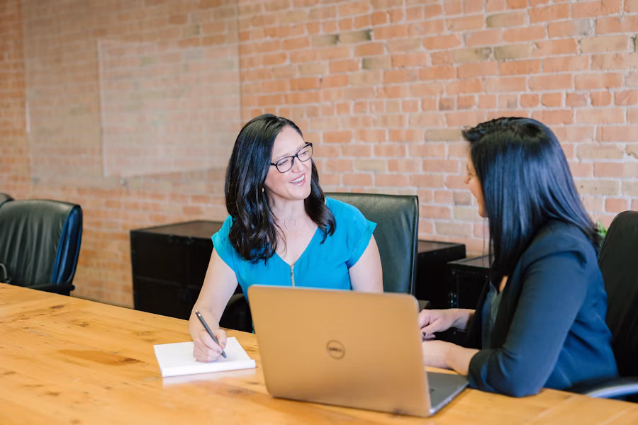 Two people talking at a desk with a laptop