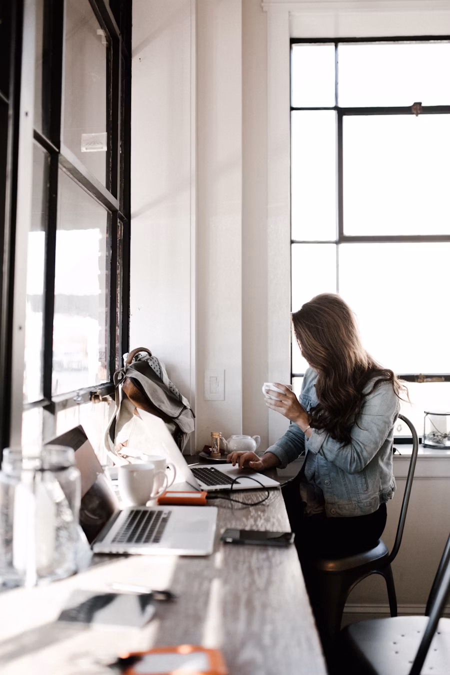 Woman by a bright window checking her laptop